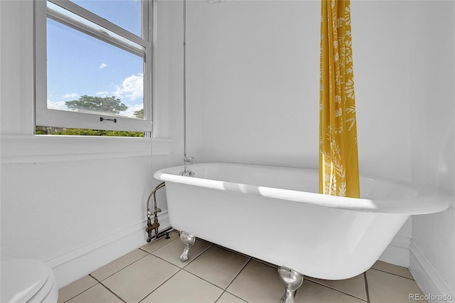 bathroom featuring toilet, a freestanding tub, tile patterned flooring, and baseboards