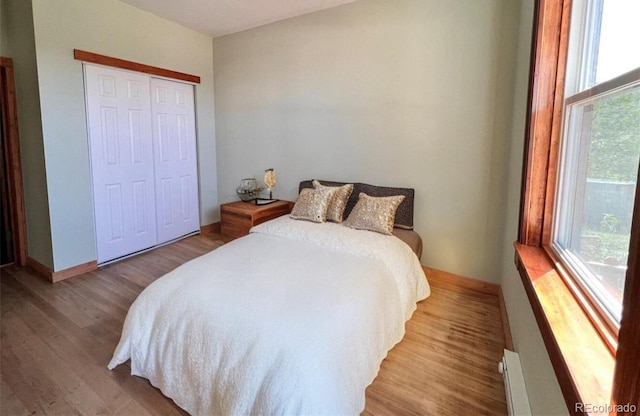 bedroom featuring a baseboard heating unit, a closet, multiple windows, and light hardwood / wood-style floors