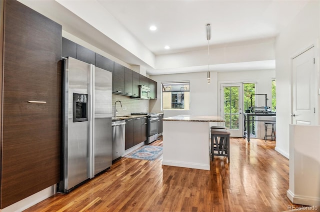 2325 Walnut St Unit 4, Denver, CO 80205 - kitchen with appliances with stainless steel finishes, a sink, wood finished floors, a kitchen breakfast bar, and decorative backsplash