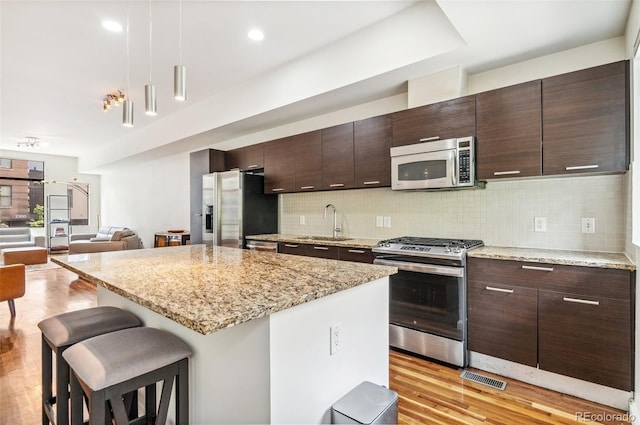 2325 Walnut St Unit 4, Denver, CO 80205 - kitchen with stainless steel appliances, a sink, a kitchen bar, light wood finished floors, and a kitchen island