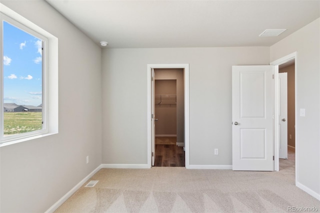 unfurnished bedroom featuring visible vents, baseboards, light colored carpet, and a spacious closet