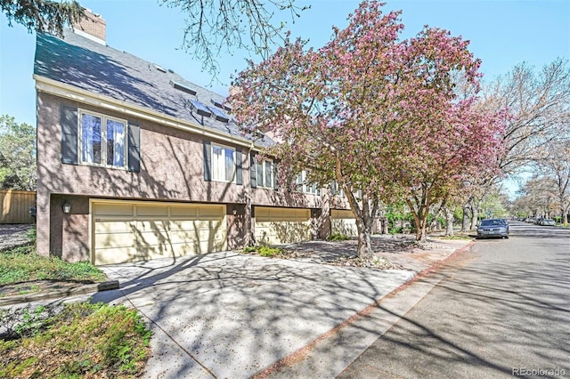 view of front facade featuring a chimney, an attached garage, driveway, and stucco siding