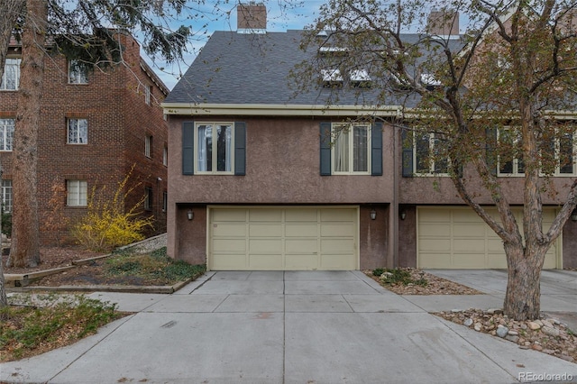 view of property with driveway, a chimney, an attached garage, a shingled roof, and stucco siding