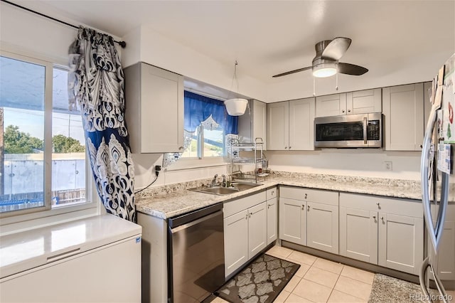 kitchen with light tile patterned floors, gray cabinetry, a sink, a ceiling fan, and appliances with stainless steel finishes