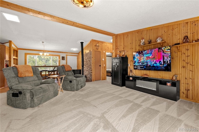 living area with carpet floors, wood walls, a textured ceiling, a glass covered fireplace, and a notable chandelier