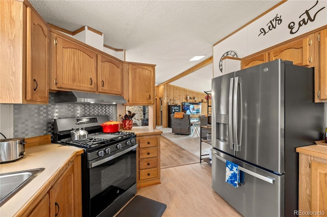 kitchen with under cabinet range hood, light countertops, appliances with stainless steel finishes, light wood-style floors, and a sink