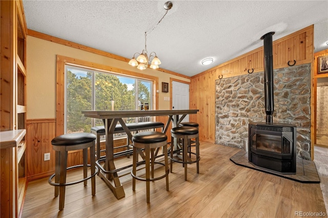 dining area featuring a wainscoted wall, wood walls, light wood-type flooring, a wood stove, and a textured ceiling