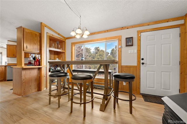 dining room with light wood-style floors, a wainscoted wall, a textured ceiling, and a notable chandelier