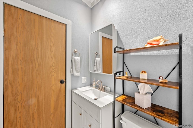 bathroom with vanity, toilet, and a textured wall