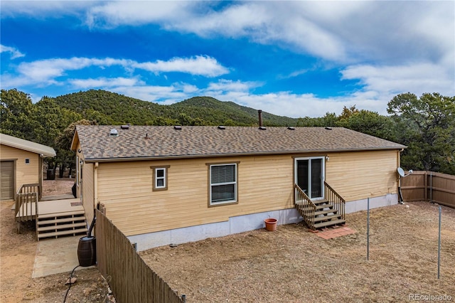 rear view of house with a deck with mountain view, entry steps, roof with shingles, and fence