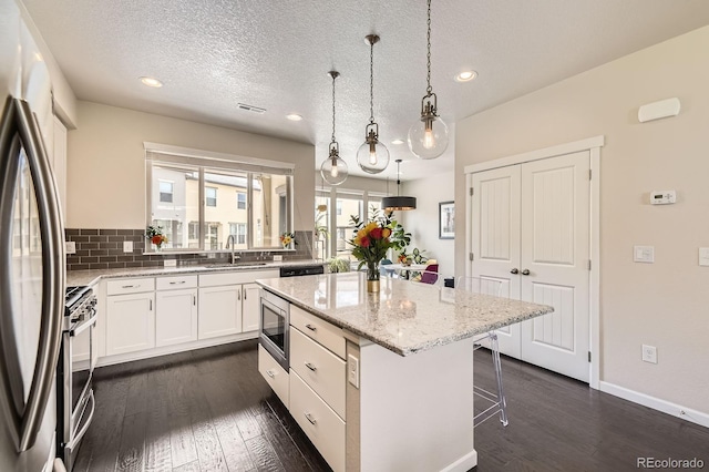 15576 W Washburn Cir, Lakewood, CO 80228 - kitchen featuring stainless steel appliances, a sink, a kitchen island, a breakfast bar, and white cabinets