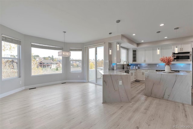 kitchen with light stone counters, decorative light fixtures, light wood-type flooring, and white cabinets