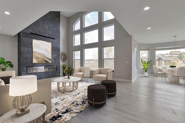 living room with light hardwood / wood-style flooring, a tiled fireplace, and high vaulted ceiling