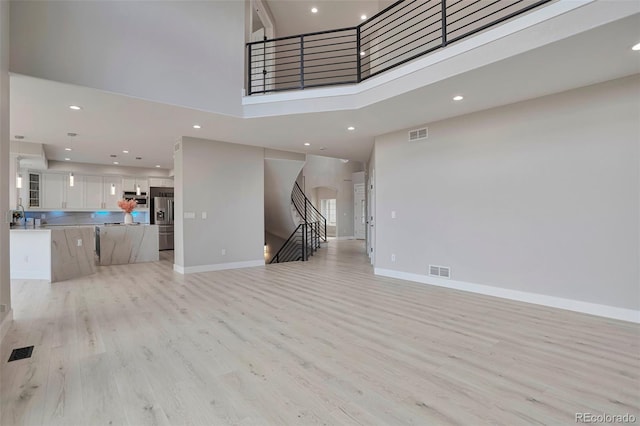 unfurnished living room featuring light hardwood / wood-style flooring and a towering ceiling