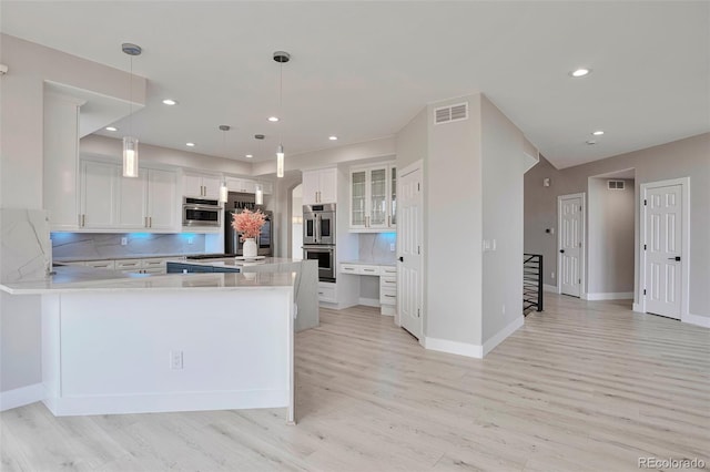 kitchen with tasteful backsplash, white cabinetry, light hardwood / wood-style floors, stainless steel appliances, and decorative light fixtures