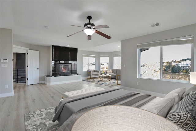 bedroom with a large fireplace, light wood-type flooring, and ceiling fan