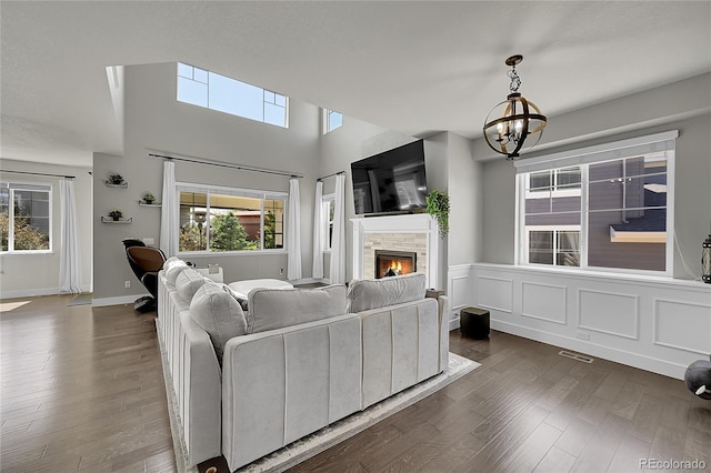 living room featuring a stone fireplace, dark hardwood / wood-style flooring, and an inviting chandelier