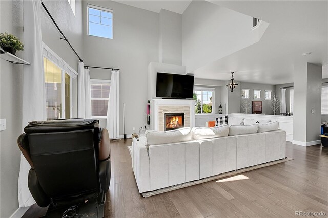 living room featuring a towering ceiling, hardwood / wood-style flooring, a notable chandelier, and a tiled fireplace