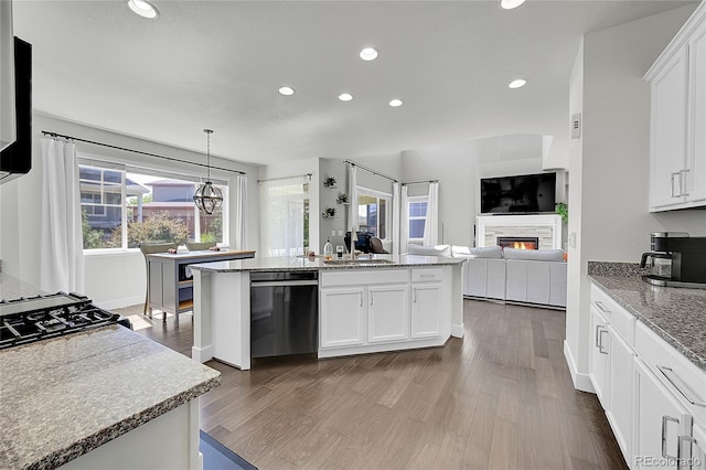 kitchen with dark hardwood / wood-style flooring, stainless steel dishwasher, an island with sink, decorative light fixtures, and white cabinets