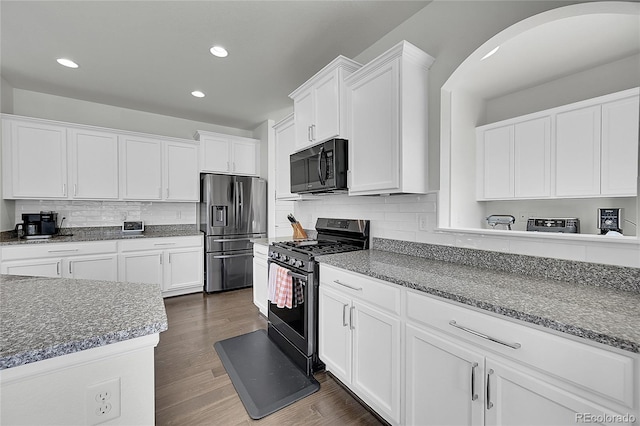 kitchen featuring dark wood-type flooring, dark stone counters, black appliances, white cabinets, and tasteful backsplash