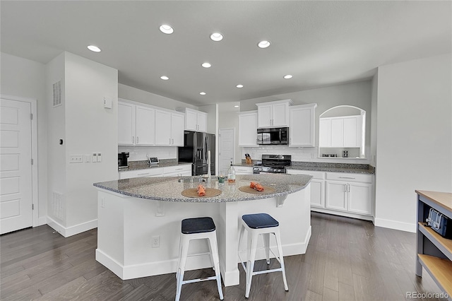 kitchen featuring white cabinets, a center island with sink, a breakfast bar area, stone countertops, and stainless steel appliances