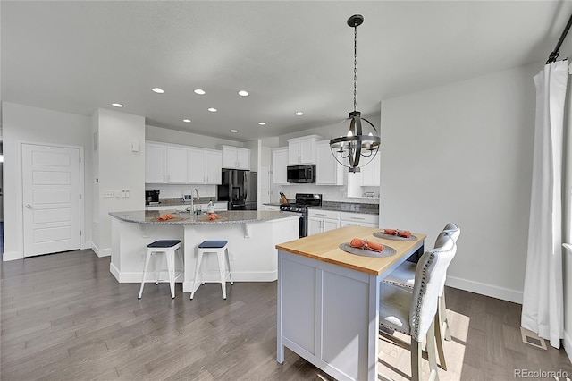 kitchen with a center island, dark stone countertops, a kitchen bar, white cabinets, and black appliances