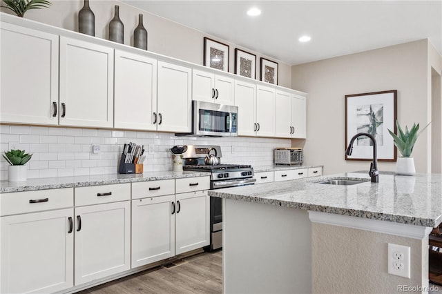 kitchen with white cabinetry, sink, a kitchen island with sink, decorative backsplash, and appliances with stainless steel finishes