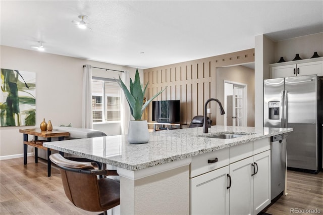 kitchen with light stone countertops, appliances with stainless steel finishes, a kitchen island with sink, sink, and white cabinets