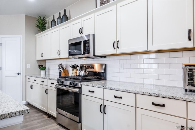 kitchen featuring tasteful backsplash, light stone counters, white cabinets, and appliances with stainless steel finishes