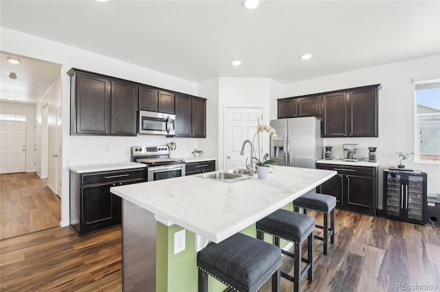 kitchen featuring a sink, stainless steel appliances, dark wood finished floors, a kitchen bar, and beverage cooler