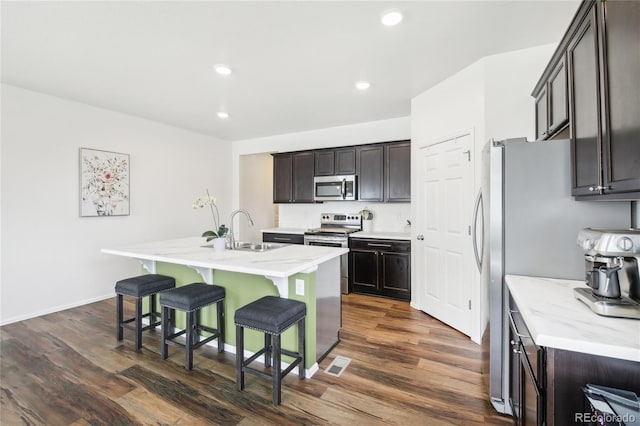kitchen featuring visible vents, a sink, a kitchen bar, appliances with stainless steel finishes, and dark wood-style floors