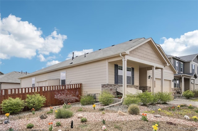 exterior space featuring covered porch, fence, an attached garage, and stone siding