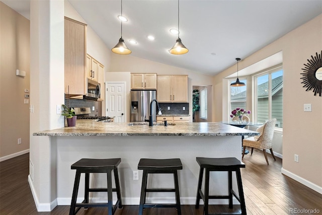 kitchen with light brown cabinetry, decorative light fixtures, appliances with stainless steel finishes, dark hardwood / wood-style floors, and kitchen peninsula