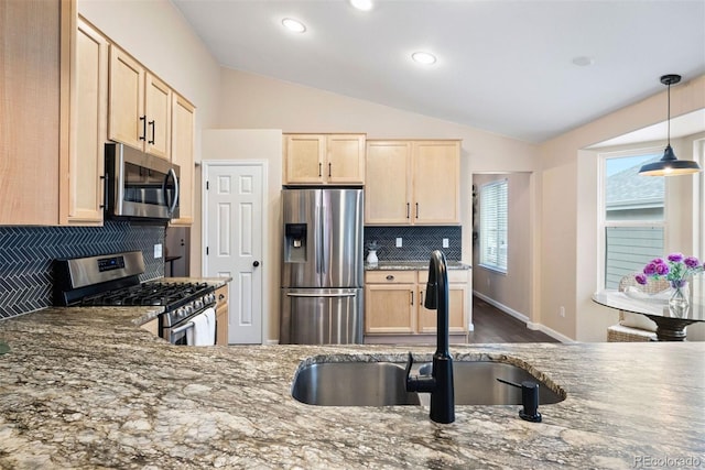 kitchen featuring stone counters, vaulted ceiling, appliances with stainless steel finishes, and sink