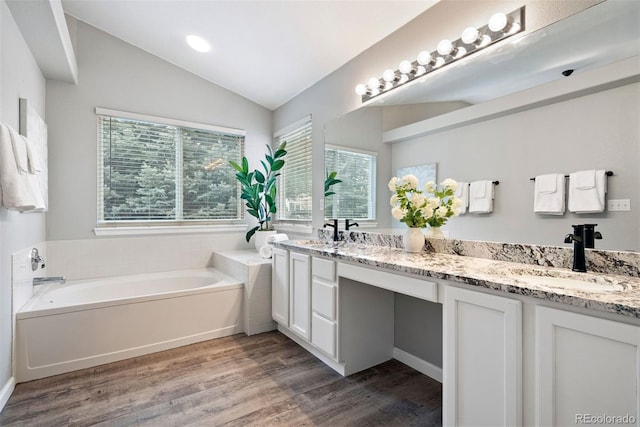 bathroom with hardwood / wood-style flooring, vanity, lofted ceiling, and a tub to relax in