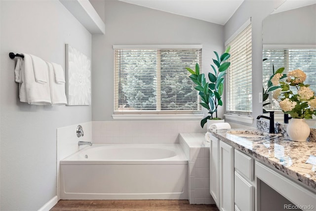 bathroom featuring vaulted ceiling, a tub, hardwood / wood-style floors, and vanity