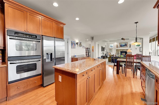 24965 E Roxbury Pl, Aurora, CO 80016 - kitchen with stainless steel appliances, a ceiling fan, a stone fireplace, a kitchen island, and light wood finished floors