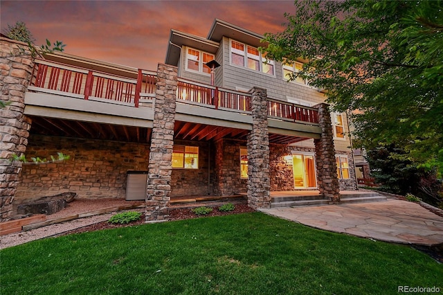 24965 E Roxbury Pl, Aurora, CO 80016 - back of property at dusk with a lawn, stone siding, and a balcony