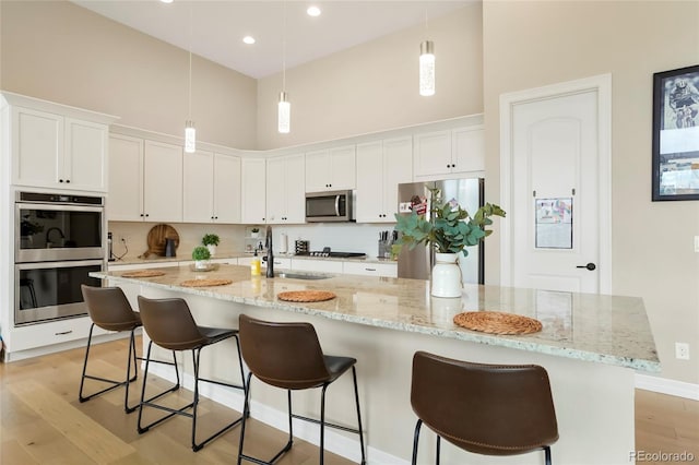 kitchen featuring stainless steel appliances, a sink, a towering ceiling, light wood-type flooring, and a large island with sink