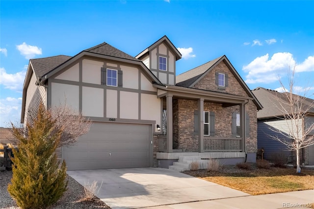 tudor-style house featuring driveway, a garage, stone siding, covered porch, and stucco siding