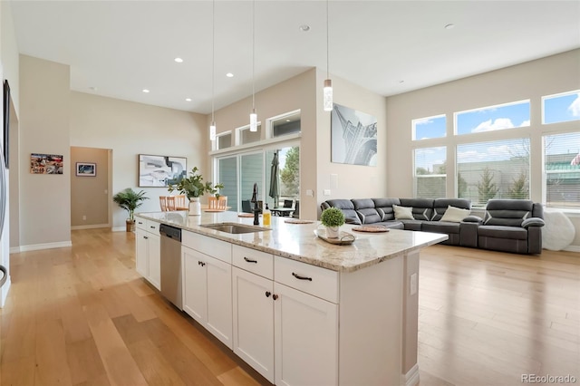 kitchen with light wood-style flooring, a sink, white cabinets, stainless steel dishwasher, and light stone countertops