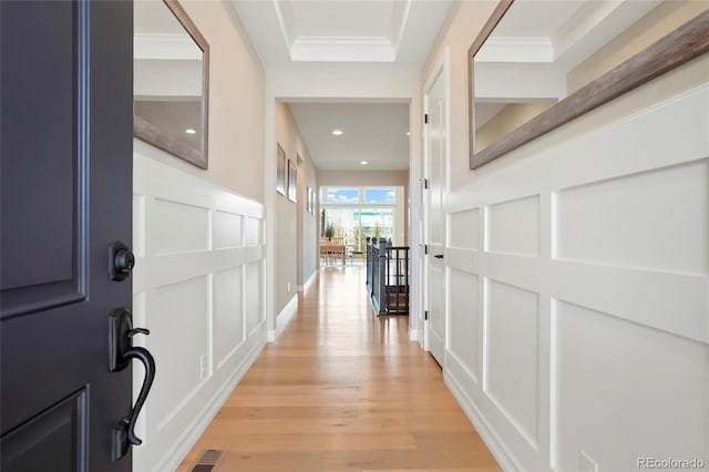 hallway featuring ornamental molding, visible vents, a decorative wall, and light wood finished floors