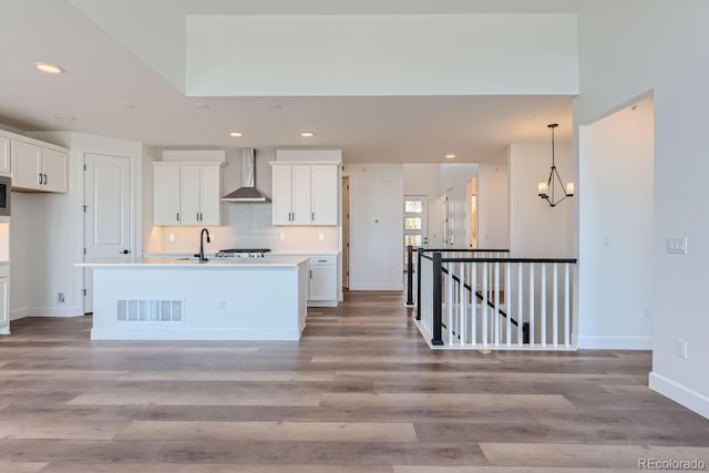 kitchen with light wood-type flooring, a center island with sink, white cabinetry, and wall chimney exhaust hood