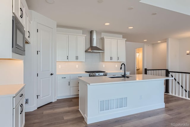 kitchen featuring white cabinetry, wall chimney range hood, and an island with sink