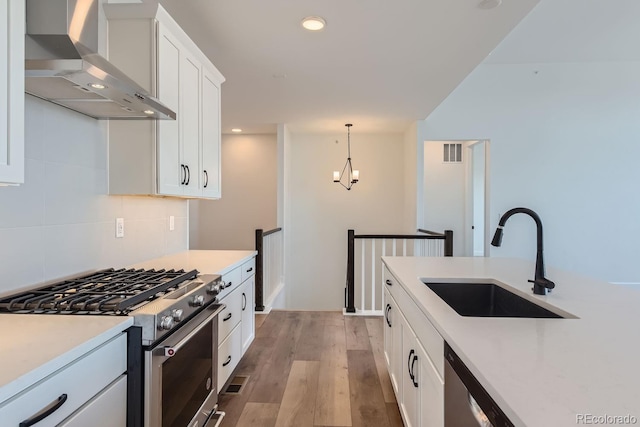 kitchen with appliances with stainless steel finishes, wall chimney exhaust hood, sink, light hardwood / wood-style flooring, and white cabinets