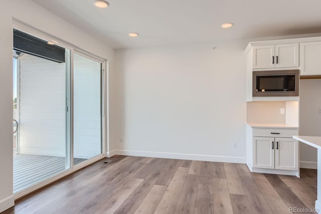 kitchen with white cabinets, light hardwood / wood-style flooring, and black microwave