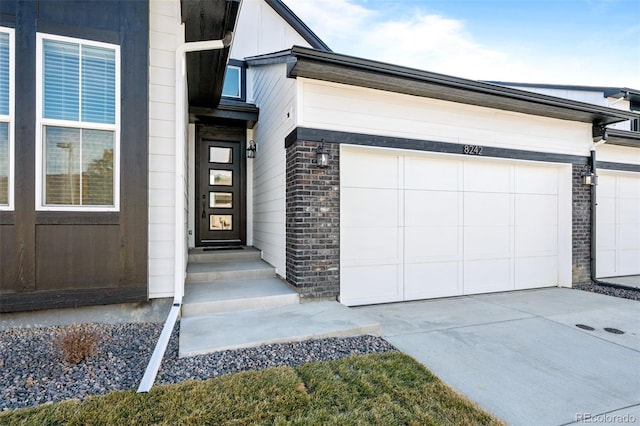 entrance to property with brick siding, an attached garage, and concrete driveway