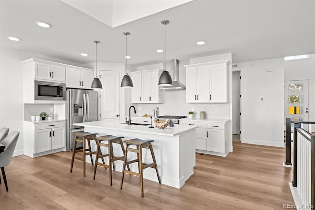 kitchen with wall chimney exhaust hood, light countertops, a center island with sink, stainless steel fridge with ice dispenser, and built in microwave