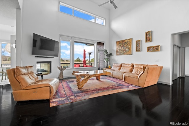 living area featuring a high ceiling, baseboards, wood finished floors, and a ceiling fan