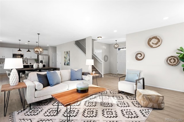 living room with recessed lighting, a notable chandelier, light wood-style flooring, and stairs